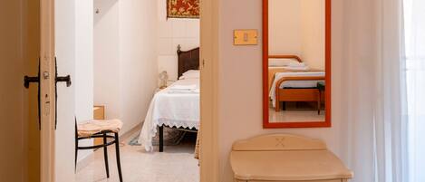 A bedroom with a bed, a chair, a bedside table, a mirror, and a wall-mounted light fixture.