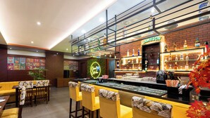 Un espace bar agrémenté d'un néon, d'une étagère où sont exposées des bouteilles d'alcool, et d'un coin salon avec des chaises jaunes.
