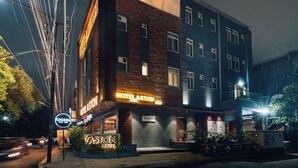 Un hôtel à plusieurs étages, reconnaissable à son grand panneau indiquant « HÔTEL ASTON », ainsi qu’à des panneaux indiquant « CAFÉ-BAR DÉCONTRACTÉ » et « HÔTEL VASTON ».