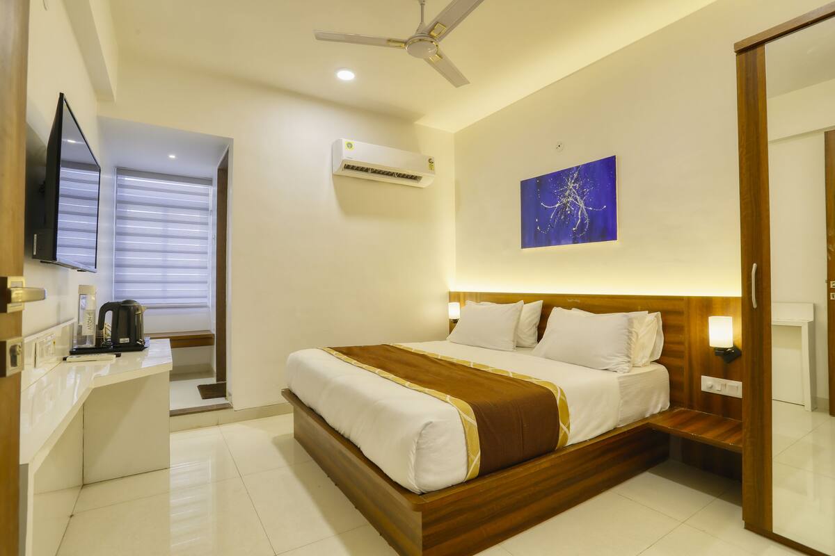 Une chambre d’hôtel équipée d’un lit, d’un bureau, d’une machine à café, d’un climatiseur, d’un ventilateur de plafond et d’un téléviseur fixé au mur.