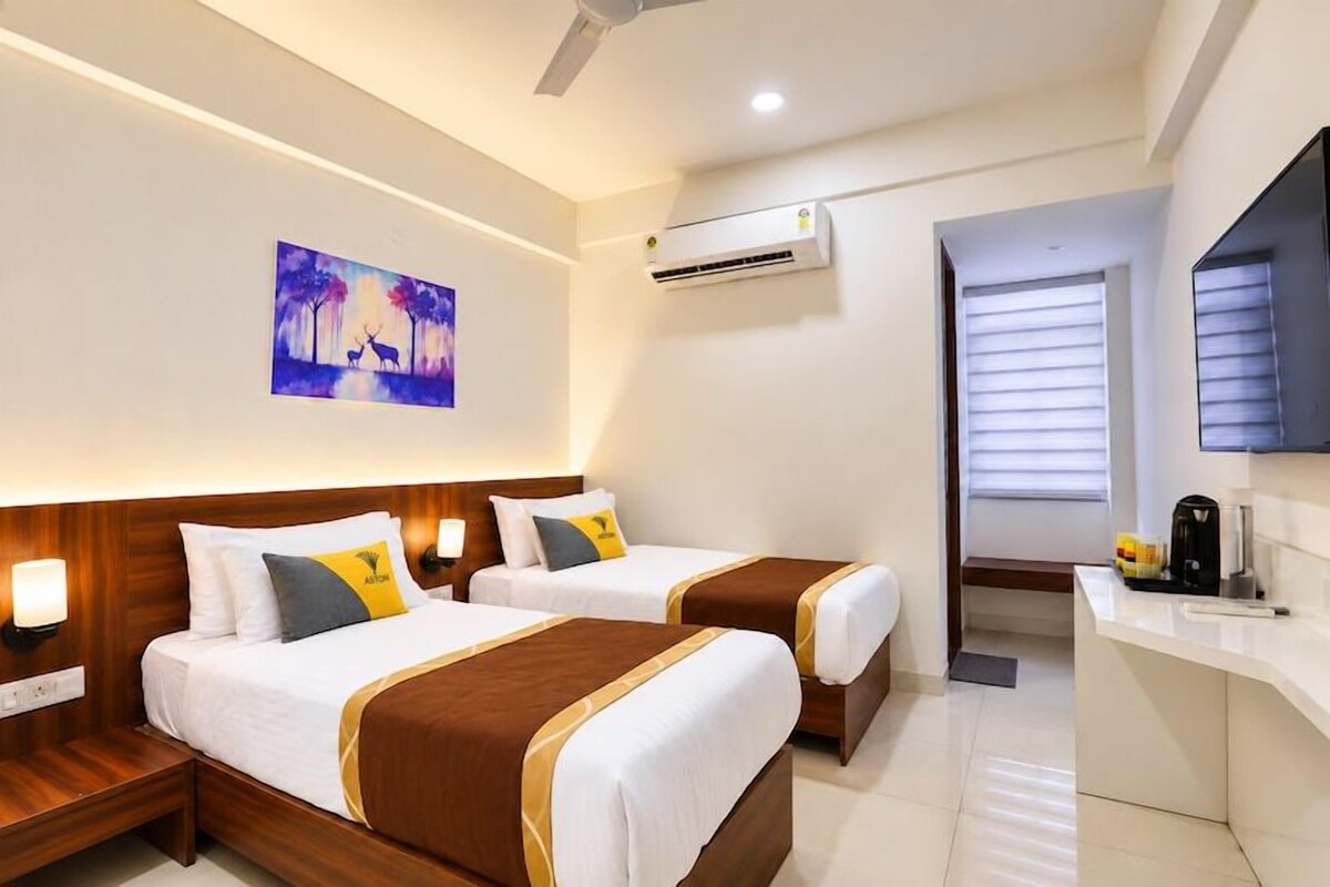 A hotel room with two beds, a desk, a chair, a TV, and an air conditioning unit.