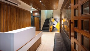 Un espace d’accueil comprenant un comptoir de réception en bois, un escalier et un mur orné de motifs géométriques.