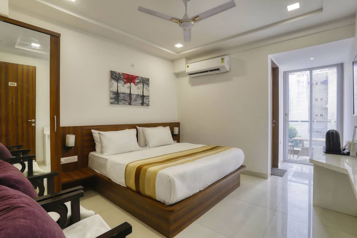 Une chambre d’hôtel avec un lit en bois, un ventilateur de plafond, un appareil de climatisation, un tableau au mur et une vue sur l’extérieur par une porte vitrée.