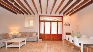 Una sala de estar con sofá, mesa de centro, mesa de comedor con sillas y techo de madera.