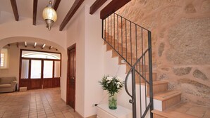 Un amplio salón con suelo de baldosas, una escalera con barandilla de metal y una pared de piedra.