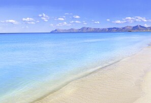 Una playa con agua azul cristalina y una cadena montañosa al fondo.