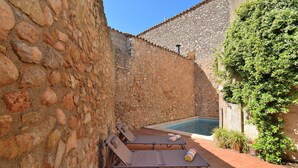Un patio con paredes de piedra, una piscina, dos sillones de descanso y plantas en macetas.