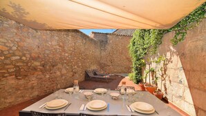 Un área de comedor al aire libre con paredes de piedra y una mesa dispuesta para seis personas, rodeada de sillas.