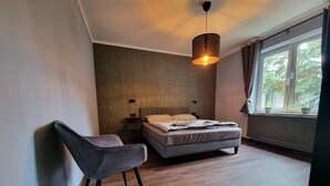 Een slaapkamer met een bed, een stoel, een hanglamp en een raam met gordijnen.