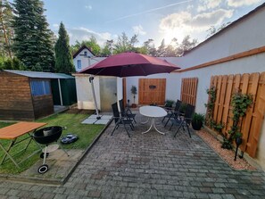 A patio with a round table and chairs, a barbecue grill, and a wooden fence. - "Ströbitzer Wiesen" Vacation Apartment (Cottbus)