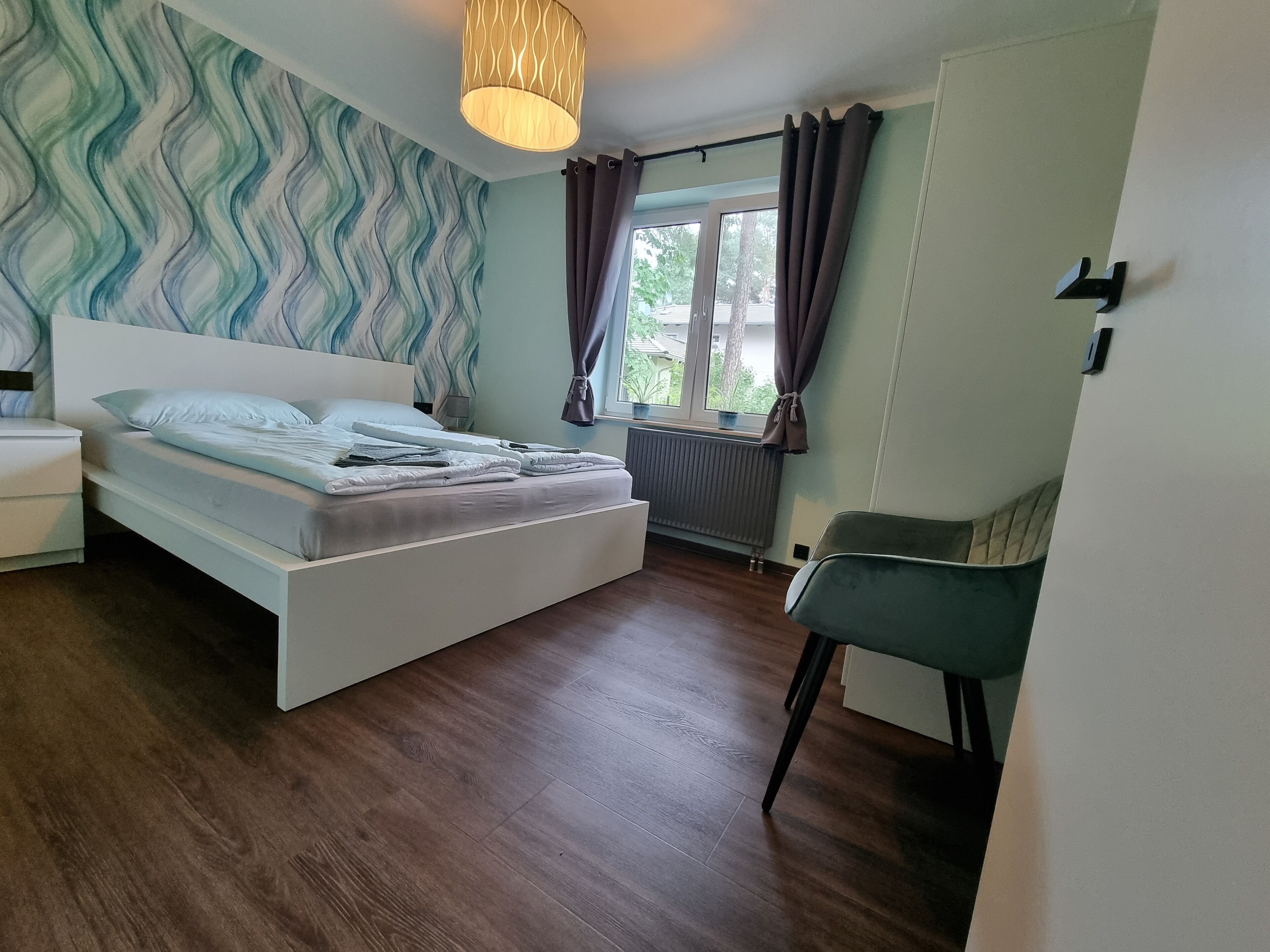 Una camera da letto con un letto, una sedia, un termosifone e una finestra con tende.
