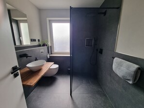 A modern bathroom with a large window, a wooden vanity, a white sink, a toilet, and a shower area. - "Ströbitzer Wiesen" Vacation Apartment (Cottbus)