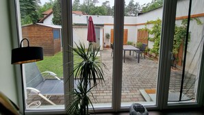 Uitzicht door een raam op een patio met een tafel, stoelen en een bloempot.