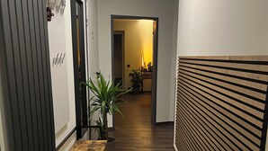 Een hal met een houten vloer, een zwarte mat, een tafel met stoelen, een potplant en een radiator.