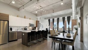 A modern kitchen with stainless steel appliances, a central island with bar stools, and a dining area with a table and chairs.