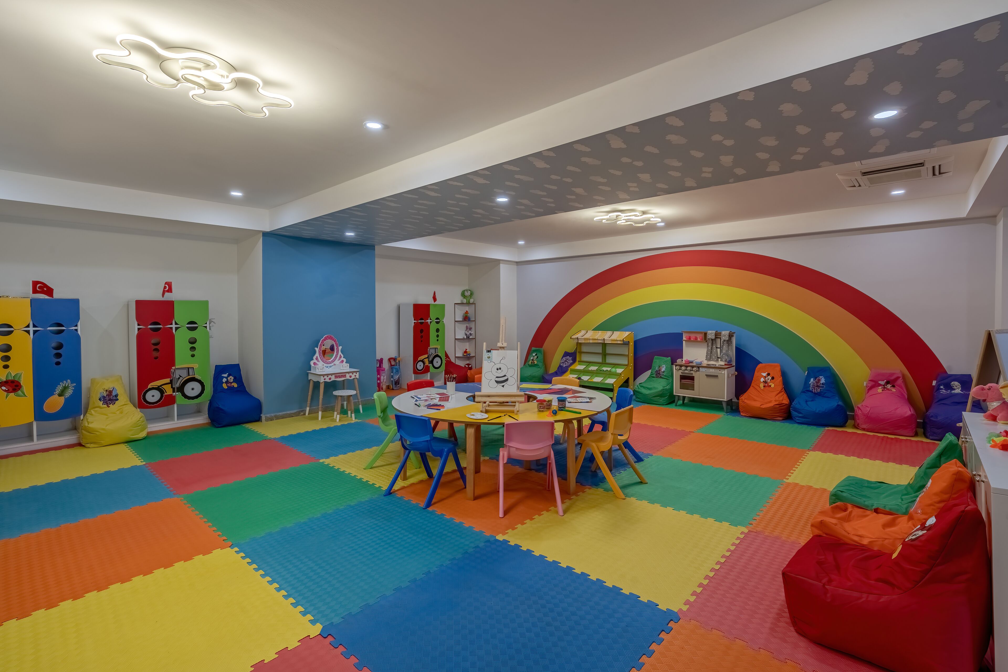 Ein Kinderspielzimmer mit bunten Matten, Sitzsäcken und Lernspielzeug.