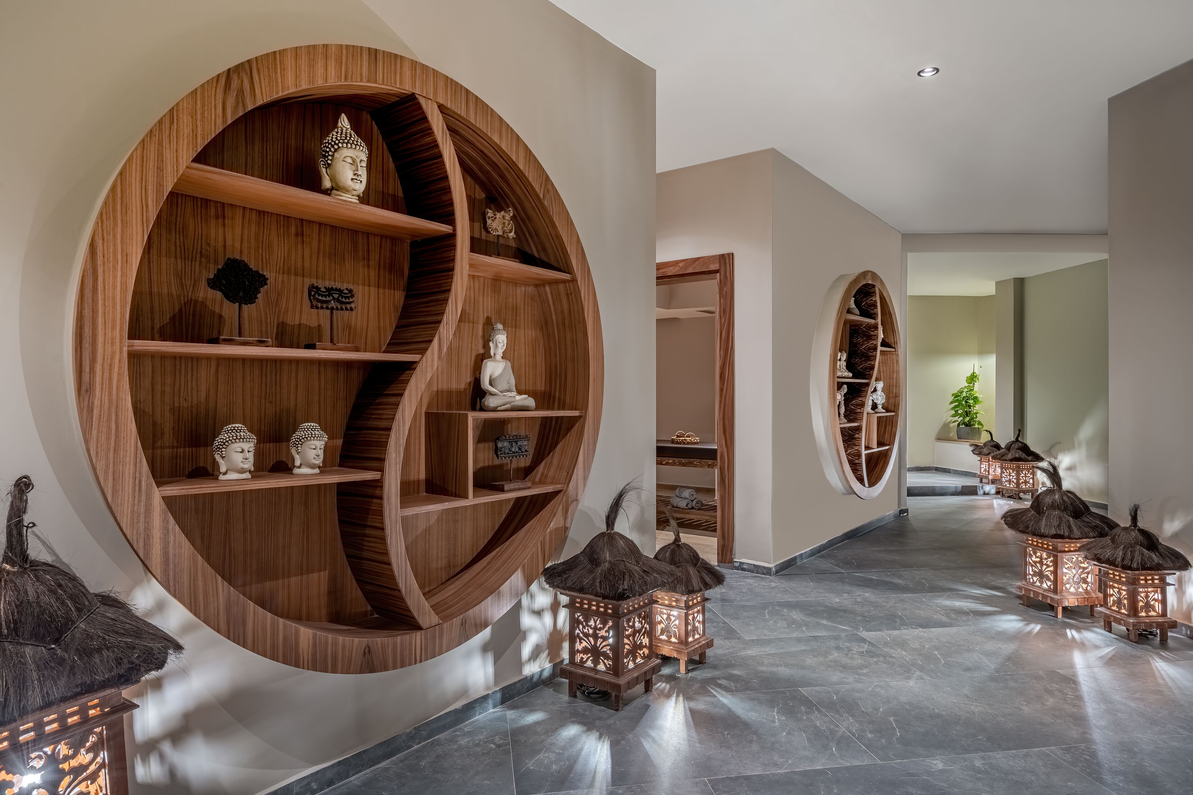 Un pasillo con estantes circulares de madera, una estatua de Buda y faroles tradicionales.