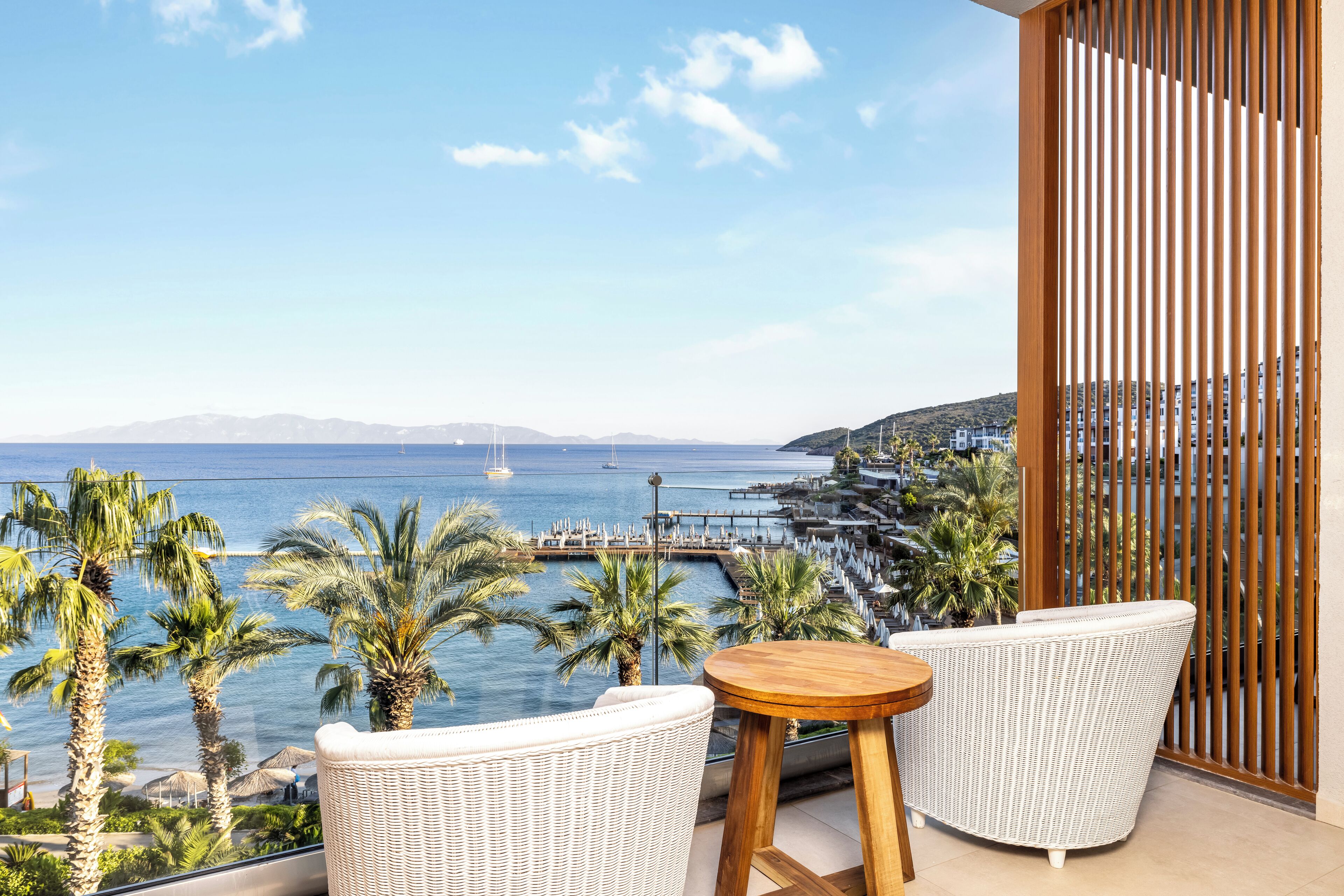 Un balcón con mobiliario de mimbre, vista al mar y valla de madera.