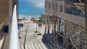 Ein Balkon mit Blick auf einen Strand und eine Meeransicht, mit einem Gebäude mit mehreren Balkonen.