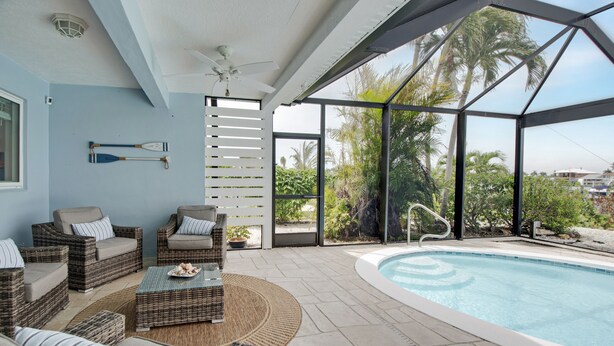 A poolside area with wicker furniture, a ceiling fan, and a view of palm trees and buildings. - CAPRI PARADISE!  Beautiful waterfront home.  Private heated pool and dock (Naples)