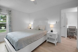 Een slaapkamer met een bed, nachtlampjes, een nachtkastje, een stoel en een deur.