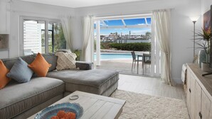 A modern living room with a grey sectional sofa, a coffee table, and a view of a pool and outdoor seating area. - CAPRI PARADISE!  Beautiful waterfront home.  Private heated pool and dock (Naples)