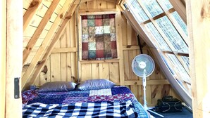 Une chambre confortable située sous les toits, avec un plafond en bois, une couvre-lit matelassé et une courtepointe accrochée au mur.