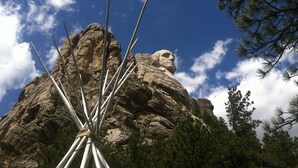 Une grande formation rocheuse surmontée d’une statue imposante, entourée d’arbres et s’ouvrant sur un ciel bleu clair.