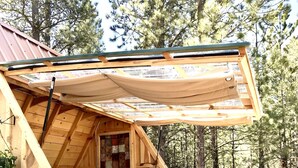 Une cabane en bois avec une chambre à coucher en mezzanine, un lit, un ventilateur et une terrasse.