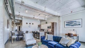 A spacious living area with a blue sofa, a round coffee table, and a dining table with chairs. A kitchen is visible in the background. - Downtown Loft: Walk to Convention (Dallas)