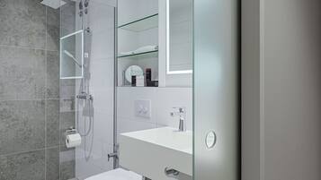 Een moderne badkamer met een douchecabine van glas, een wit toilet en een wastafel met spiegel.