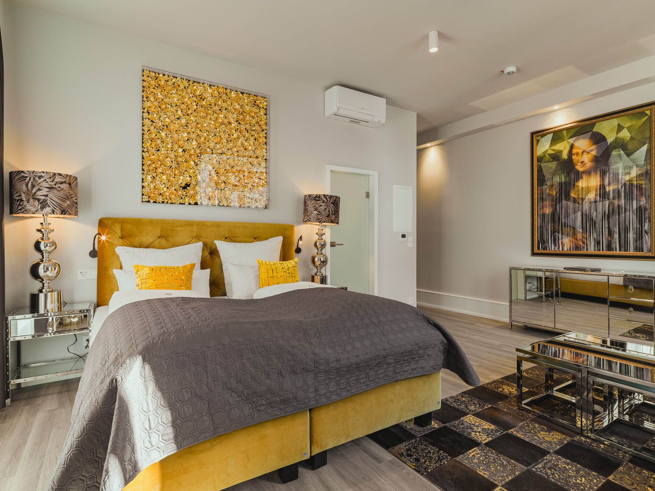A modern bedroom with a large bed, a headboard, a wall-mounted air conditioner, and a painting.