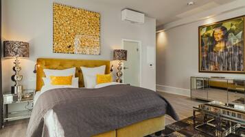 A modern bedroom with a large bed, a headboard, a wall-mounted air conditioner, and a painting.