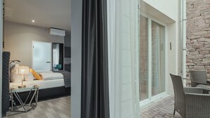 A modern hotel room with a bed, a small table, and a chair. There is a balcony with wicker furniture and a stone wall. - BS Boutique Hotel (Heidelberg)