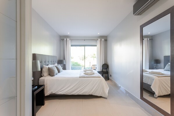 Un dormitorio moderno con una cama grande, una mesita de noche, una silla y un espejo amplio.
