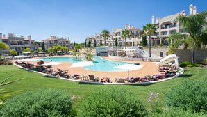 Un resort con piscina central, varias zonas de descanso y un césped cuidado.