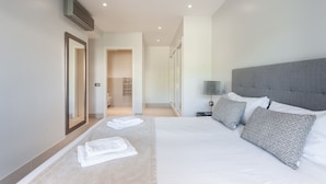 Habitación de hotel moderna con una cama grande, una mesita de noche con lámpara y vista al pasillo.