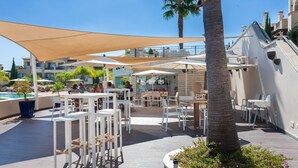 Un patio al aire libre con mesas, sillas, piscina y palmeras.