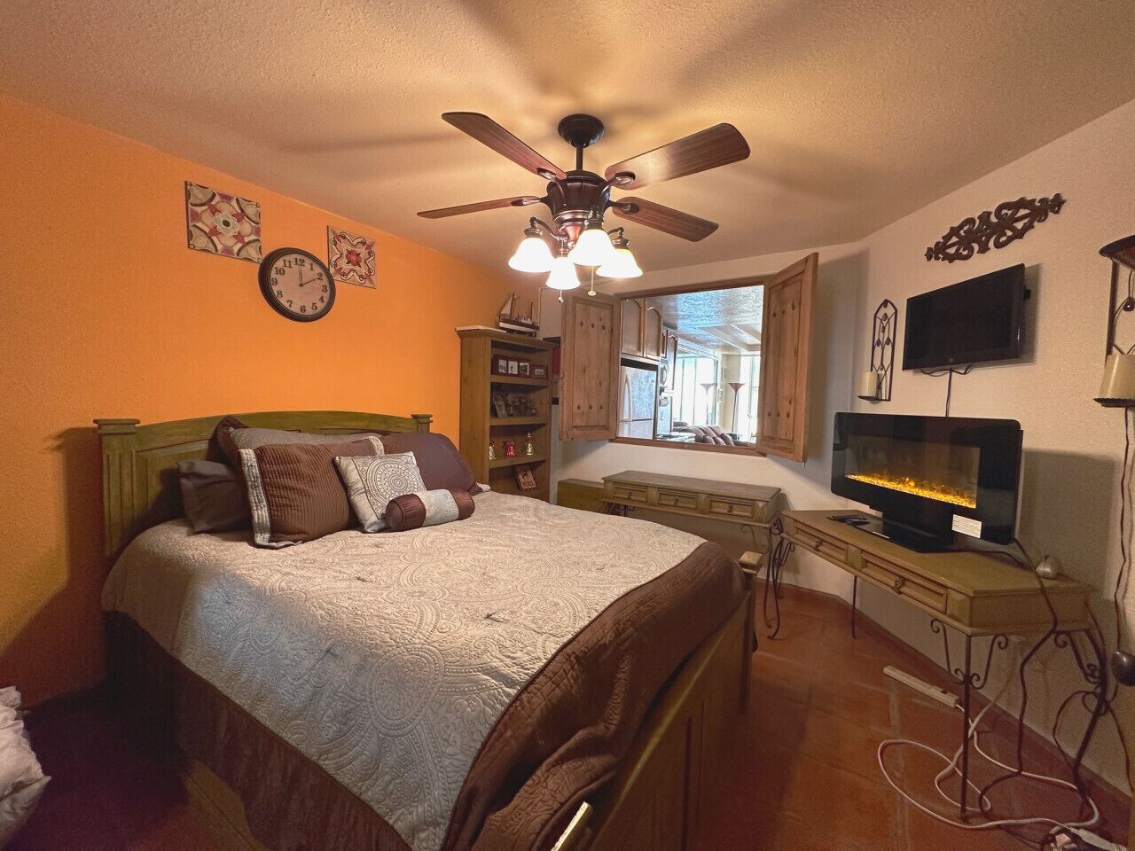 A bedroom with a bed, a ceiling fan, a TV, and a window.