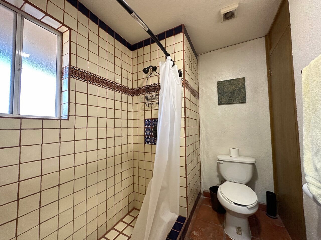 A bathroom with a shower, toilet, and a window.