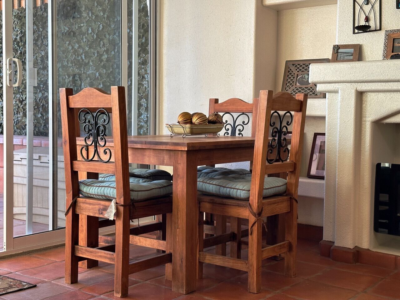 A wooden dining table with four chairs, a bowl of decorative items, and a fireplace in the background.