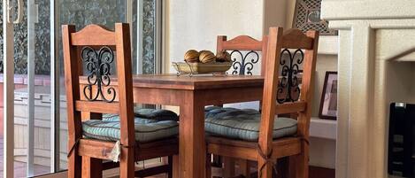 A wooden dining table with four chairs, a bowl of decorative items, and a fireplace in the background.