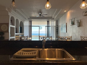 A kitchen with a sink, a ceiling fan, and a view of the ocean through large windows. - Rosarito Oceanfront Penthouse: Pool, Spa & Views in Costa Bella (Rosarito)