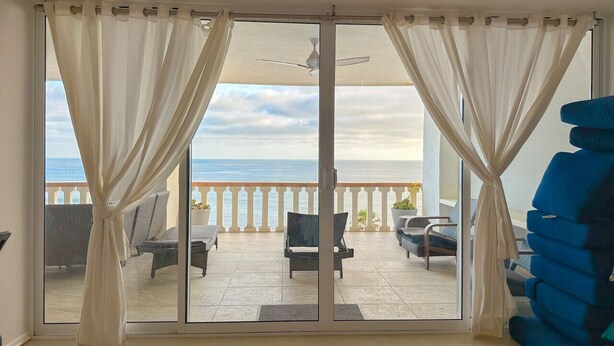 A room with a balcony overlooking the sea, featuring a ceiling fan, a sofa, and a chair. - Coastal luxury paradise (Rosarito)