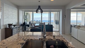 A modern kitchen with a large island, a dining area, and a view of the ocean. - Coastal luxury paradise (Rosarito)