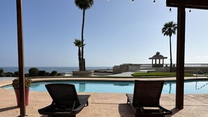 A poolside area with two lounge chairs, a palm tree, and a view of the ocean. - Coastal luxury paradise (Rosarito)
