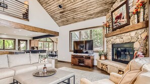 Amplia sala de estar con chimenea de piedra, televisor y un gran ventanal.