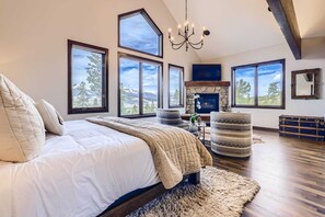 A spacious bedroom with a large bed, multiple windows, a fireplace, and a chandelier.