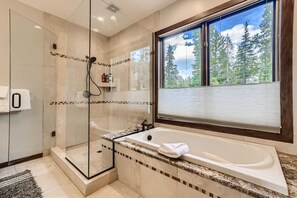 Un bagno moderno con doccia vetrata, una vasca da bagno ampia e una finestra con vista sulla foresta.