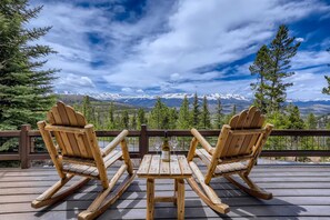 Due poltrone Adirondack su un pontile in legno con un tavolo, vista su un paesaggio montuoso.